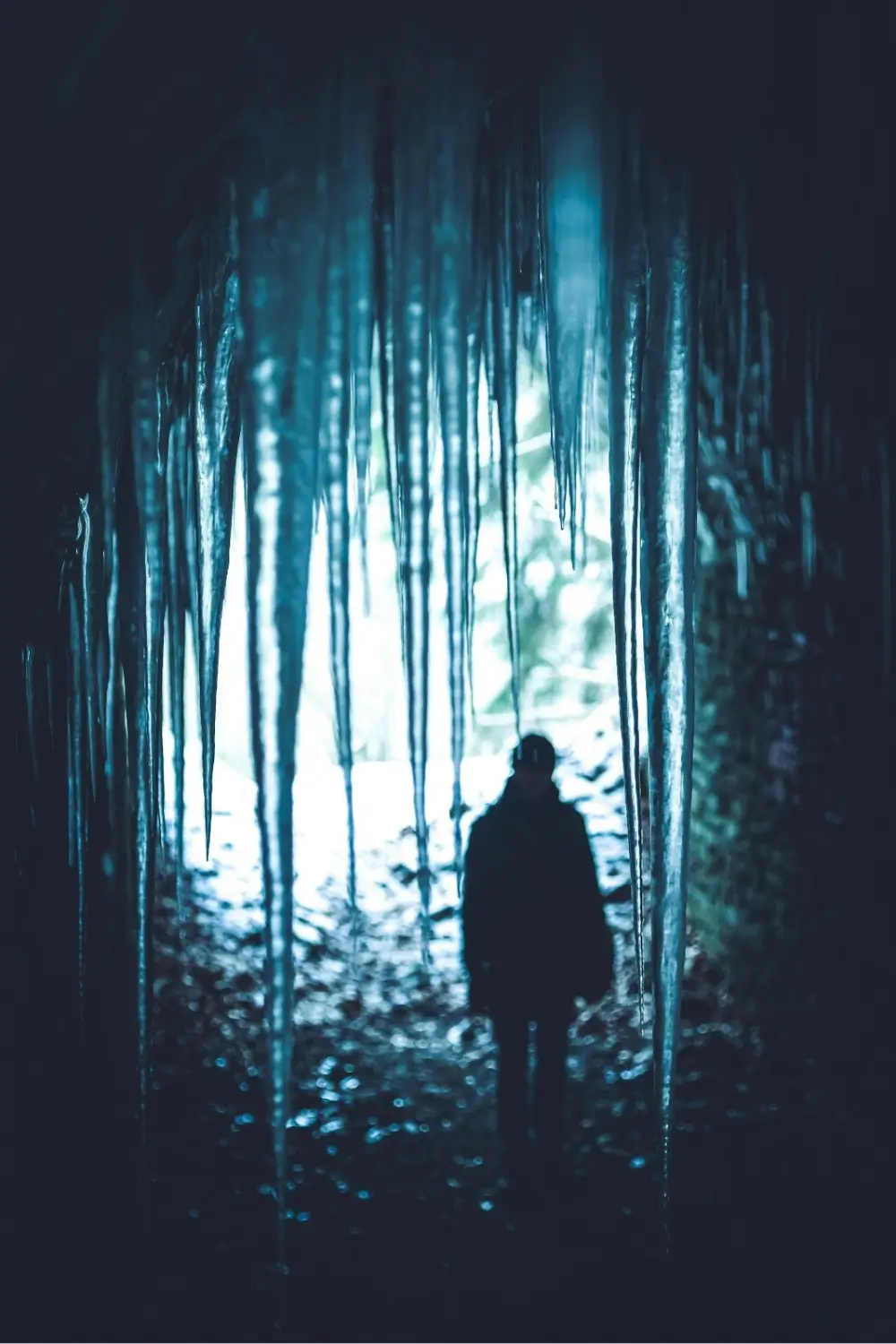 Pessoa em pé diante da luz ao fim de uma caverna escura, simbolizando o despertar da humanidade esquecida.