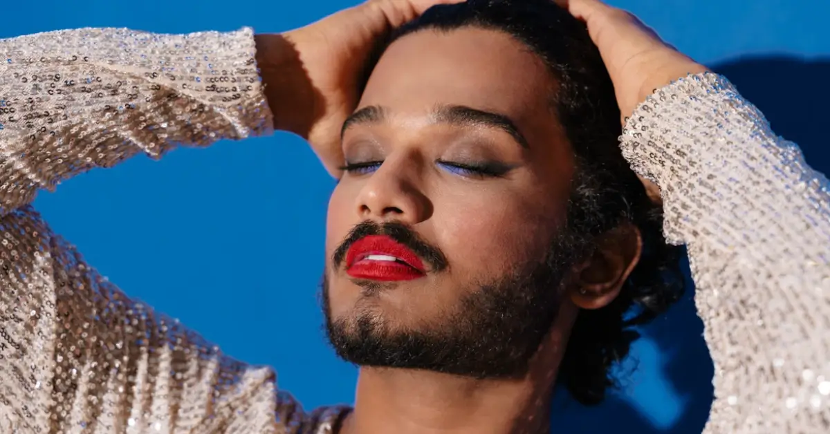 Pessoa com expressão andrógina, usando maquiagem colorida e roupa com brilho, simbolizando liberdade de identidade de gênero e o uso de pronomes neutros é uma questão de respeito à diversidade.